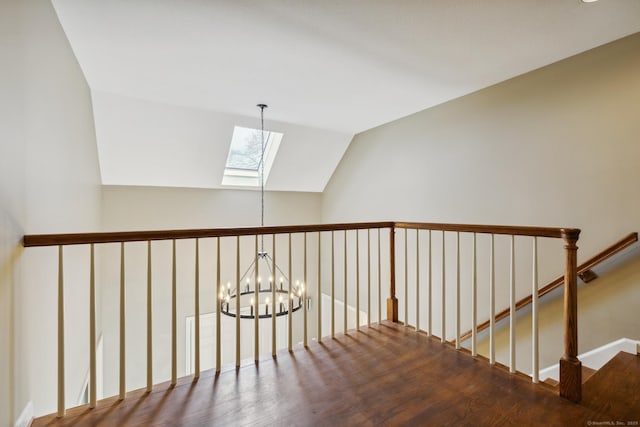corridor featuring a notable chandelier, wood finished floors, lofted ceiling with skylight, and an upstairs landing
