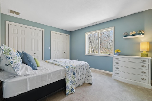 bedroom with baseboards, visible vents, two closets, and light colored carpet