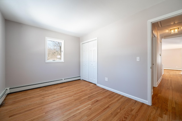 unfurnished bedroom with baseboard heating, a closet, and light wood-type flooring