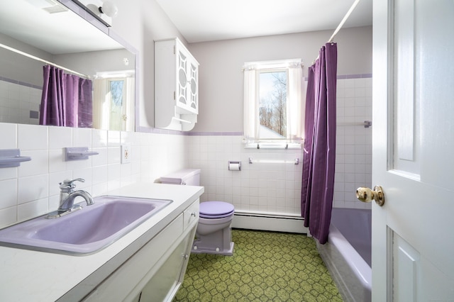 full bathroom with toilet, shower / tub combo with curtain, tile walls, baseboard heating, and vanity