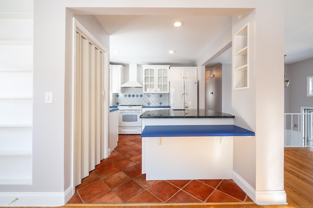 kitchen with wall chimney exhaust hood, white cabinetry, decorative backsplash, white appliances, and a breakfast bar area