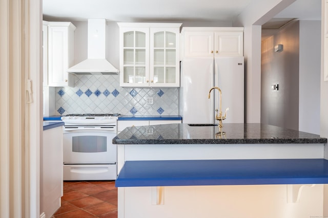 kitchen featuring white appliances, a kitchen bar, tasteful backsplash, wall chimney range hood, and white cabinets