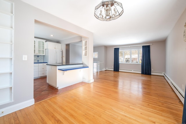 kitchen with a baseboard heating unit, tasteful backsplash, white cabinetry, light hardwood / wood-style floors, and white fridge