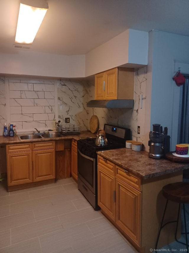 kitchen featuring dark stone countertops, gas range, decorative backsplash, and a kitchen bar