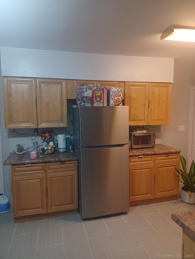 kitchen featuring stainless steel refrigerator, light tile patterned floors, and dark stone countertops