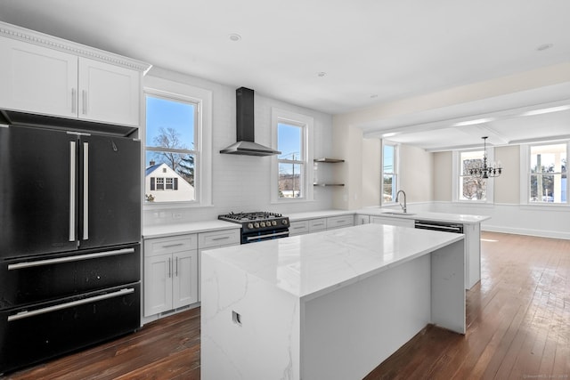 kitchen featuring high end appliances, white cabinetry, wall chimney range hood, sink, and dark hardwood / wood-style floors