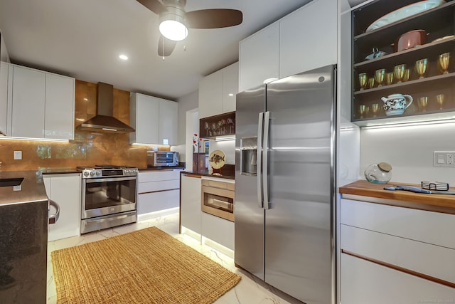 kitchen with wall chimney exhaust hood, backsplash, white cabinets, light tile patterned floors, and stainless steel appliances