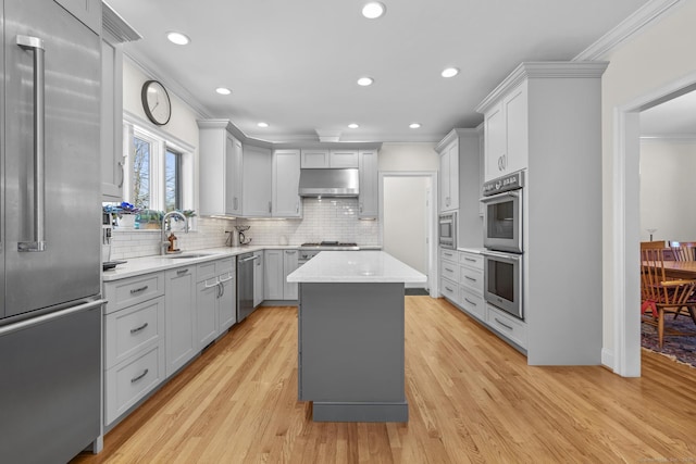 kitchen featuring built in appliances, under cabinet range hood, light countertops, ornamental molding, and light wood finished floors