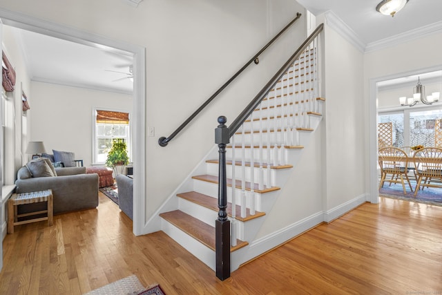 staircase with ceiling fan with notable chandelier, baseboards, crown molding, and wood finished floors