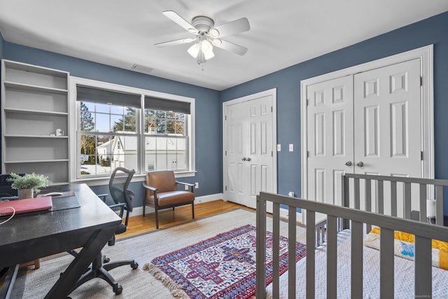 interior space with visible vents, baseboards, ceiling fan, wood finished floors, and two closets