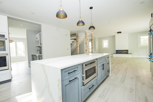 kitchen with sink, light stone counters, decorative light fixtures, an island with sink, and white cabinets