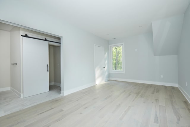 unfurnished bedroom featuring a barn door, light hardwood / wood-style floors, and a closet