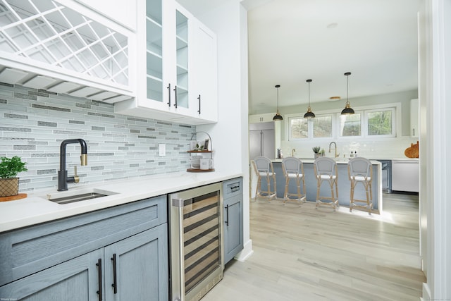 kitchen with gray cabinets, sink, wine cooler, decorative backsplash, and hanging light fixtures