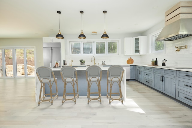 kitchen with wall chimney range hood, decorative backsplash, white cabinets, decorative light fixtures, and stainless steel built in fridge