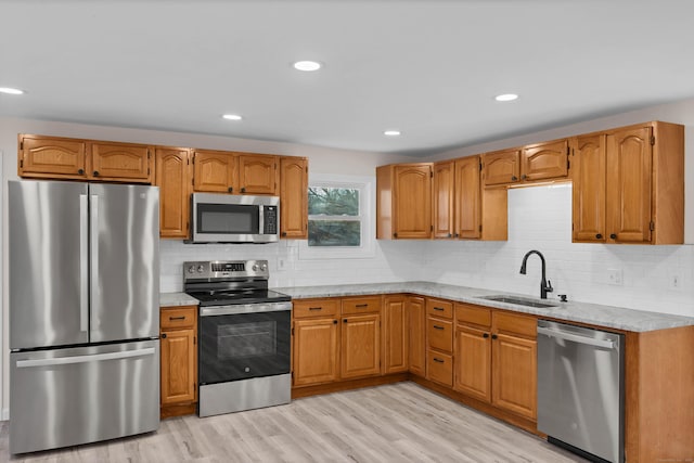 kitchen with light stone countertops, appliances with stainless steel finishes, tasteful backsplash, sink, and light hardwood / wood-style flooring