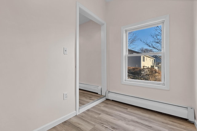 unfurnished room featuring a baseboard radiator, a wealth of natural light, and light wood-type flooring