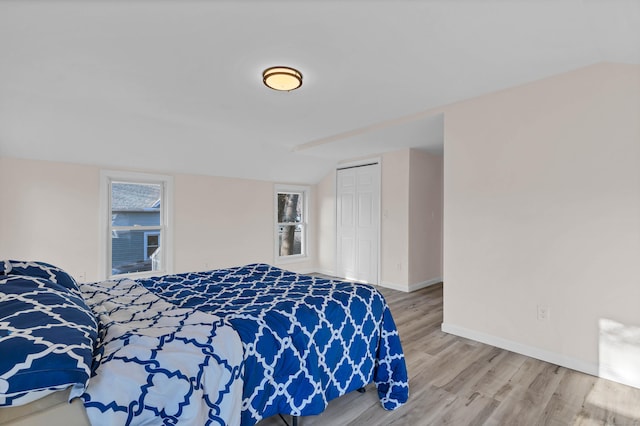 bedroom with multiple windows, wood-type flooring, a closet, and lofted ceiling