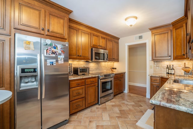 kitchen with stainless steel appliances, light stone countertops, sink, and backsplash