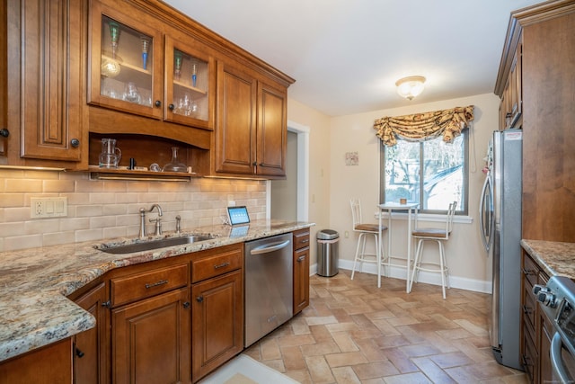 kitchen with stainless steel appliances, sink, light stone counters, and decorative backsplash