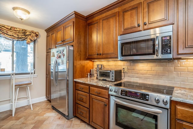 kitchen featuring light stone counters, decorative backsplash, and stainless steel appliances