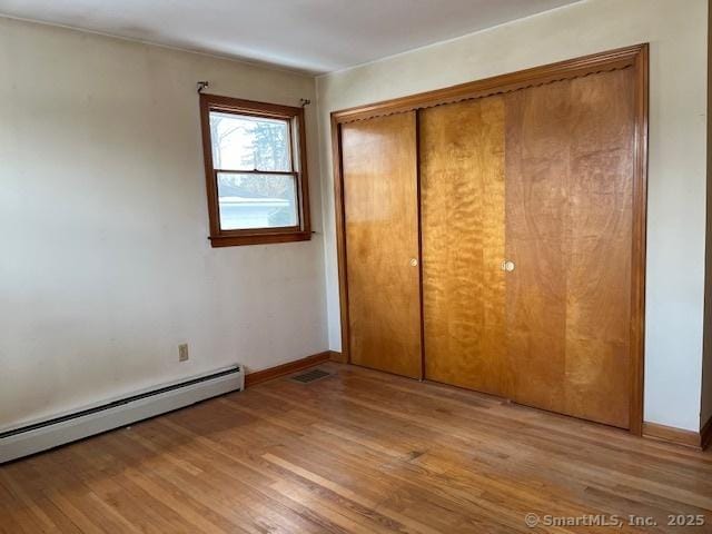 unfurnished bedroom featuring light hardwood / wood-style floors, a closet, and baseboard heating