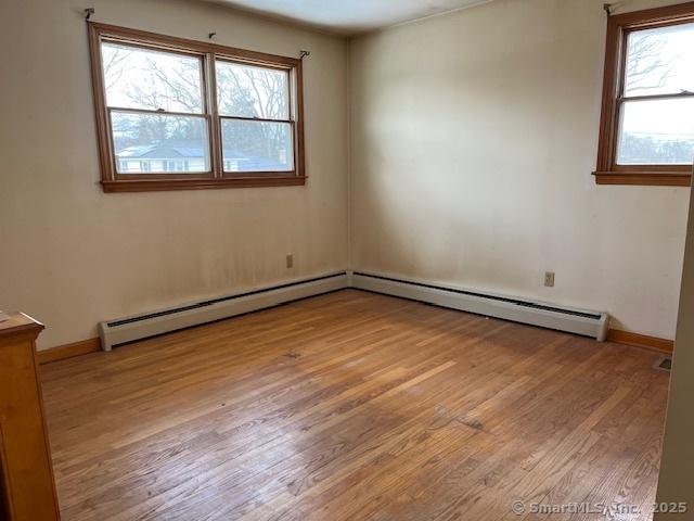 empty room with baseboard heating, a healthy amount of sunlight, and light hardwood / wood-style flooring