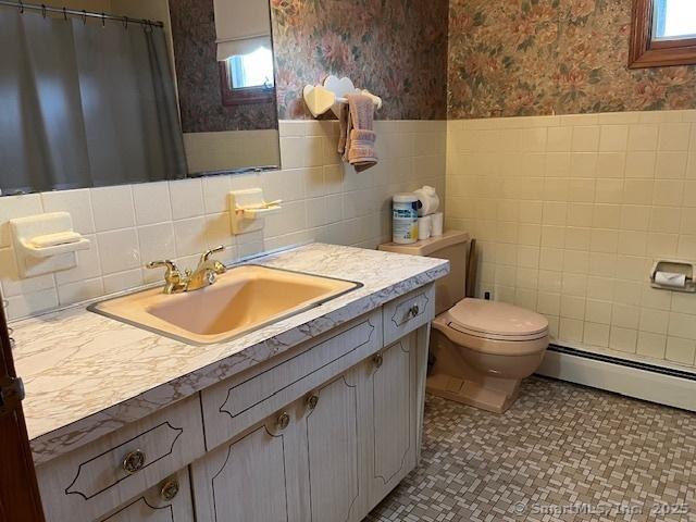 bathroom featuring a baseboard heating unit, vanity, a healthy amount of sunlight, and toilet