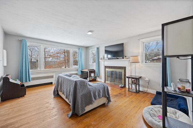 living room featuring radiator heating unit, a brick fireplace, and light hardwood / wood-style flooring