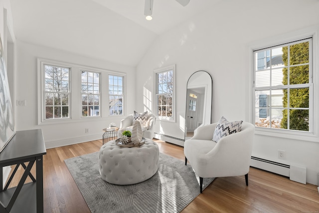 sitting room with vaulted ceiling, a baseboard radiator, wood-type flooring, and a healthy amount of sunlight