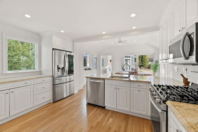 kitchen with sink, light hardwood / wood-style flooring, appliances with stainless steel finishes, white cabinets, and vaulted ceiling