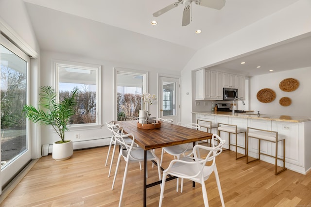 dining space with vaulted ceiling, sink, a baseboard radiator, and light hardwood / wood-style floors