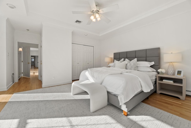 bedroom with ornamental molding, a raised ceiling, a closet, ceiling fan, and light hardwood / wood-style floors