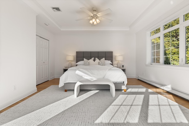 bedroom featuring a baseboard heating unit, a tray ceiling, ceiling fan, and light wood-type flooring