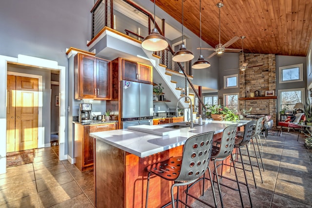 kitchen featuring high vaulted ceiling, hanging light fixtures, stainless steel fridge, and a center island with sink