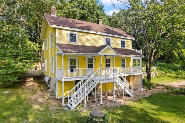 view of front of house featuring covered porch, a chimney, a front yard, and stairs