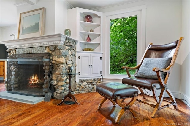 living area with ornamental molding, a fireplace, wood finished floors, and baseboards