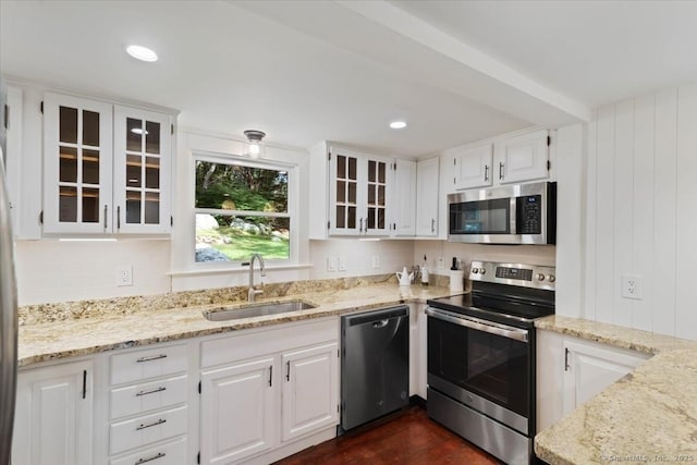 kitchen with stainless steel appliances, light stone counters, a sink, and white cabinetry