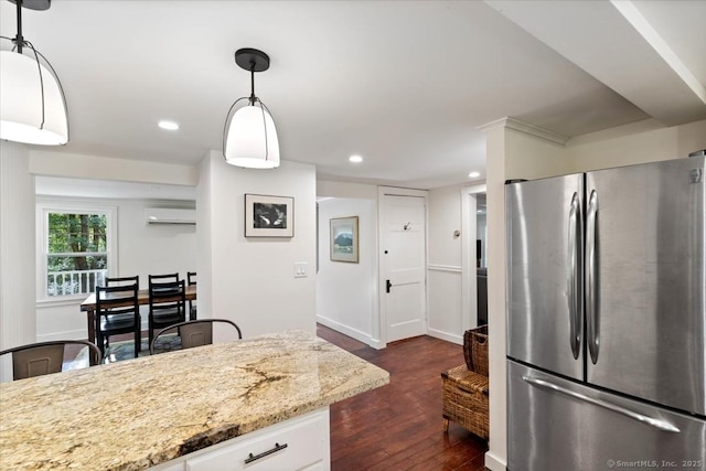 kitchen with light stone counters, an AC wall unit, hanging light fixtures, freestanding refrigerator, and dark wood-style floors