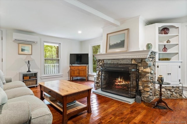 living room featuring beam ceiling, a wall mounted AC, ornamental molding, a stone fireplace, and wood finished floors