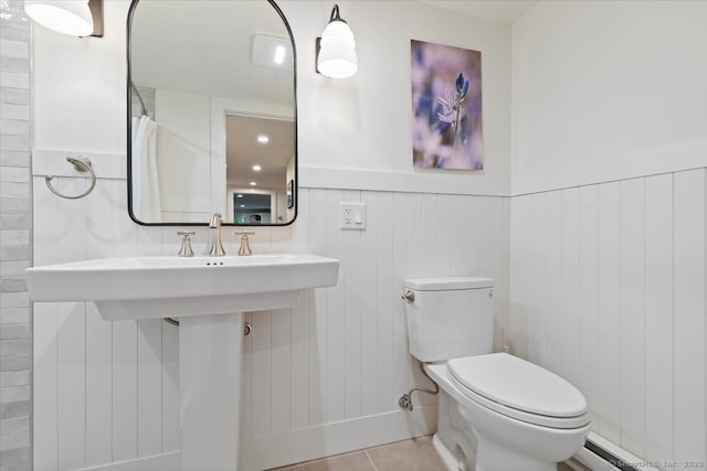 bathroom featuring a wainscoted wall, a baseboard heating unit, tile patterned flooring, and toilet