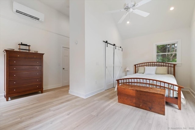 bedroom featuring a barn door, high vaulted ceiling, light wood-type flooring, a wall mounted air conditioner, and baseboards