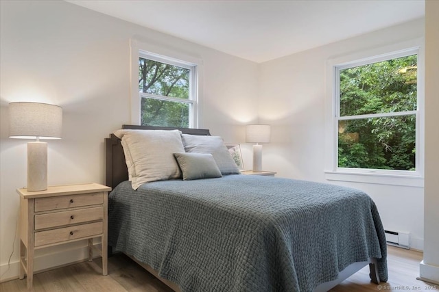 bedroom with a baseboard heating unit and light wood finished floors