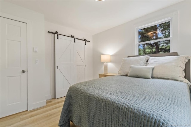 bedroom with light wood-type flooring, a barn door, and baseboards