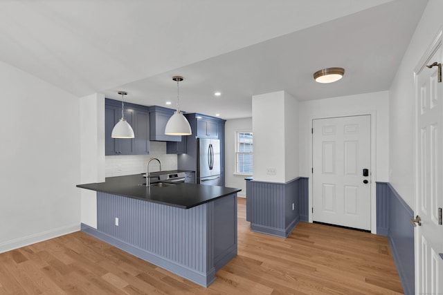 kitchen featuring appliances with stainless steel finishes, blue cabinets, decorative light fixtures, kitchen peninsula, and light wood-type flooring