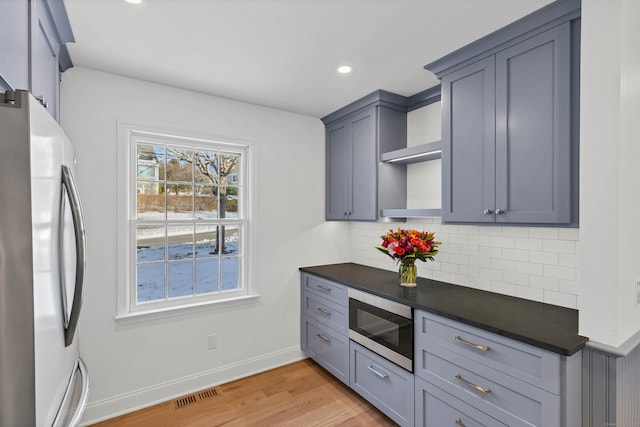 kitchen with gray cabinetry, appliances with stainless steel finishes, light hardwood / wood-style floors, and backsplash