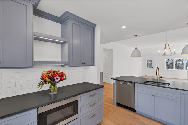 kitchen with sink, decorative light fixtures, light wood-type flooring, appliances with stainless steel finishes, and decorative backsplash