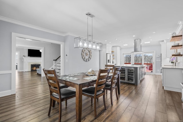 dining room with a warm lit fireplace, baseboards, ornamental molding, dark wood-style flooring, and stairs