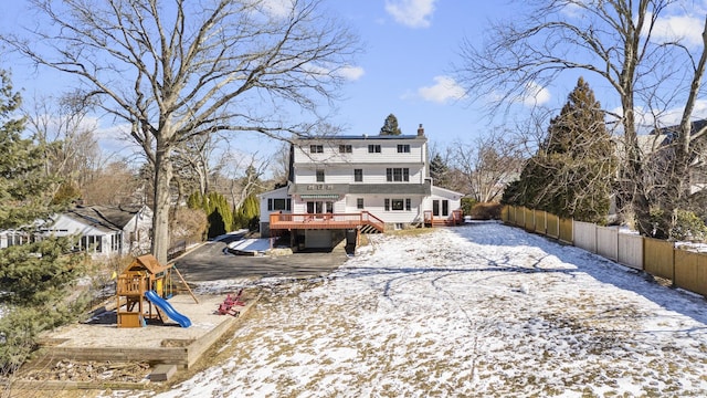 snow covered property featuring a chimney, fence, a playground, and a wooden deck