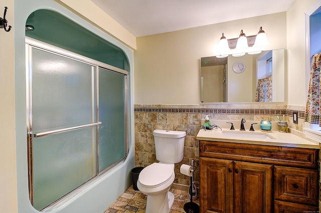 full bathroom featuring toilet, vanity, enclosed tub / shower combo, and tile walls