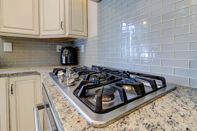 interior details featuring light stone countertops, backsplash, and stainless steel gas stovetop